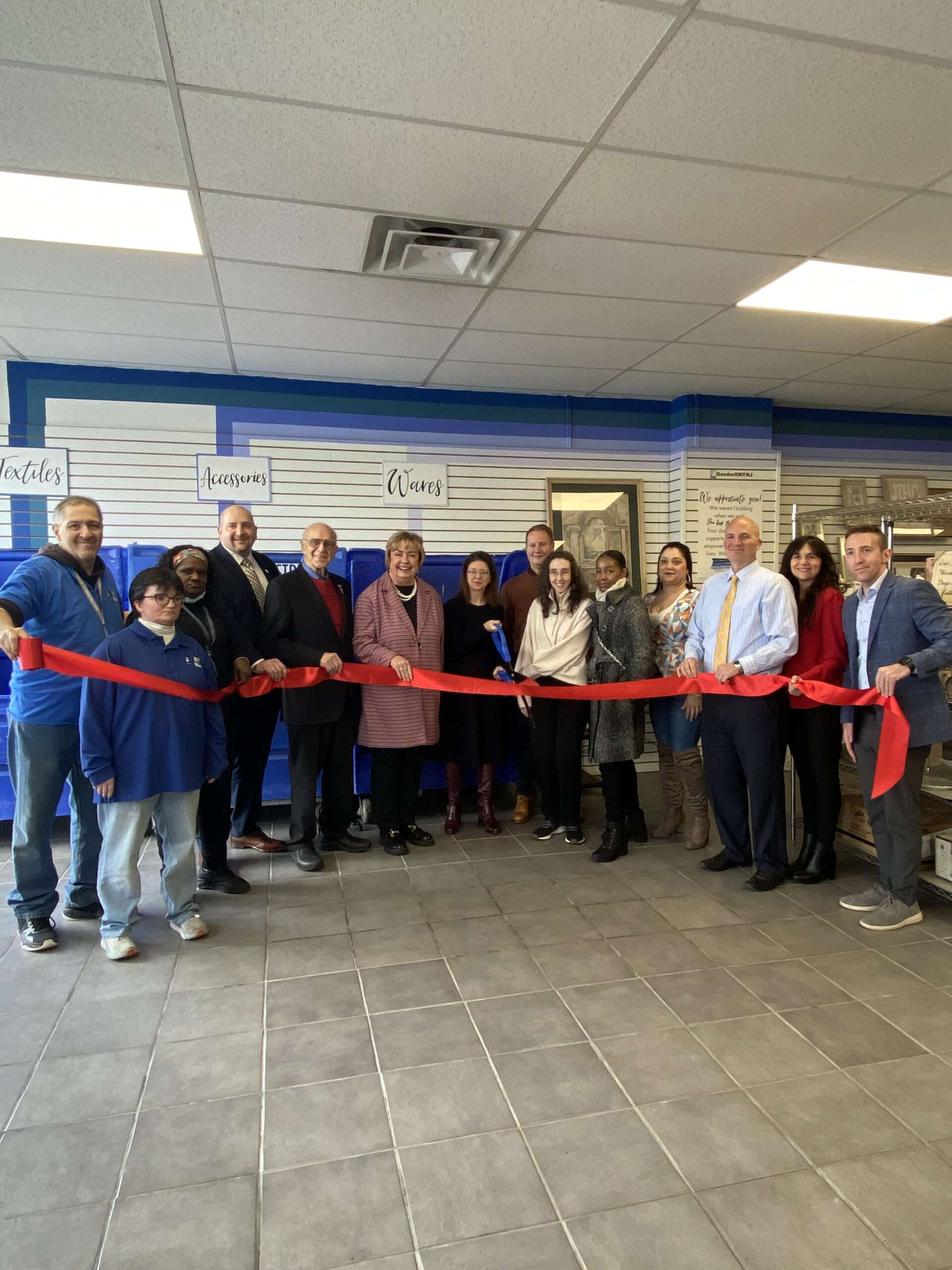 Group at a store ribbon-cutting ceremony with oversized scissors, ready to cut a red ribbon.